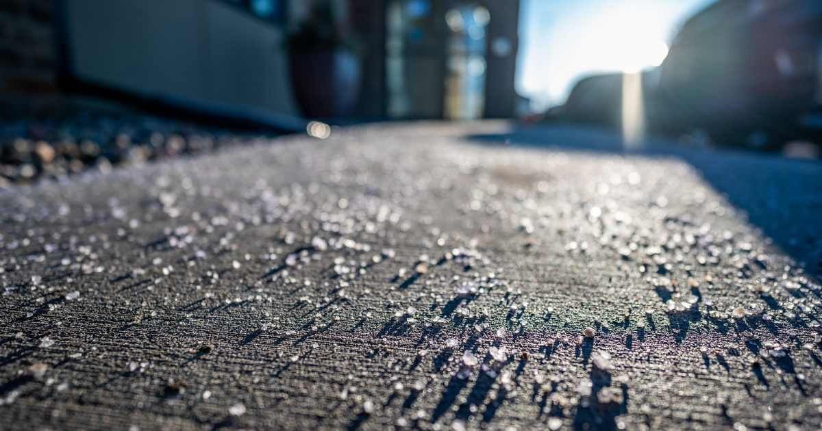 Close-up view of rock salt scattered on a concrete sidewalk on a sunny winter day.